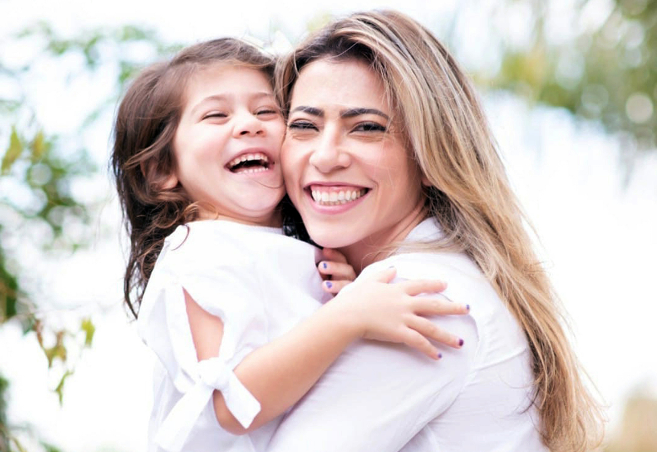 Mother and daughter with their faces close together, smiling at the camera, both wearing white T-shirts.