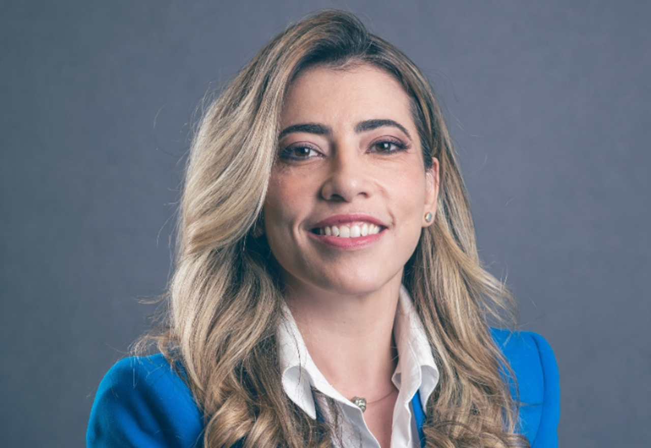 A blonde-haired white woman smiling at the camera, wearing a blue blazer over a white shirt.