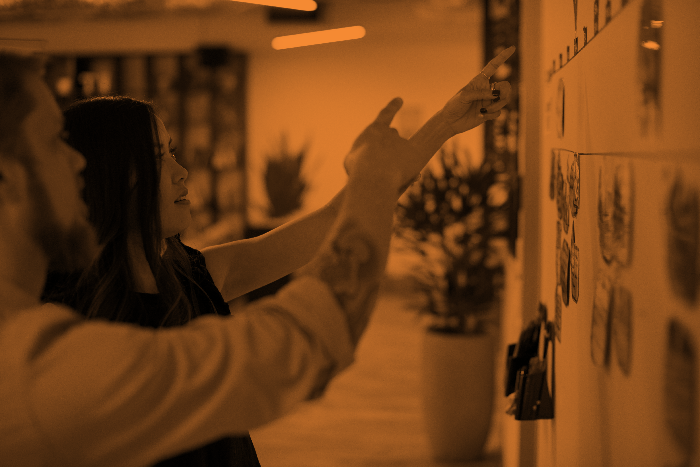 Hands point at post it notes lining a user story wall